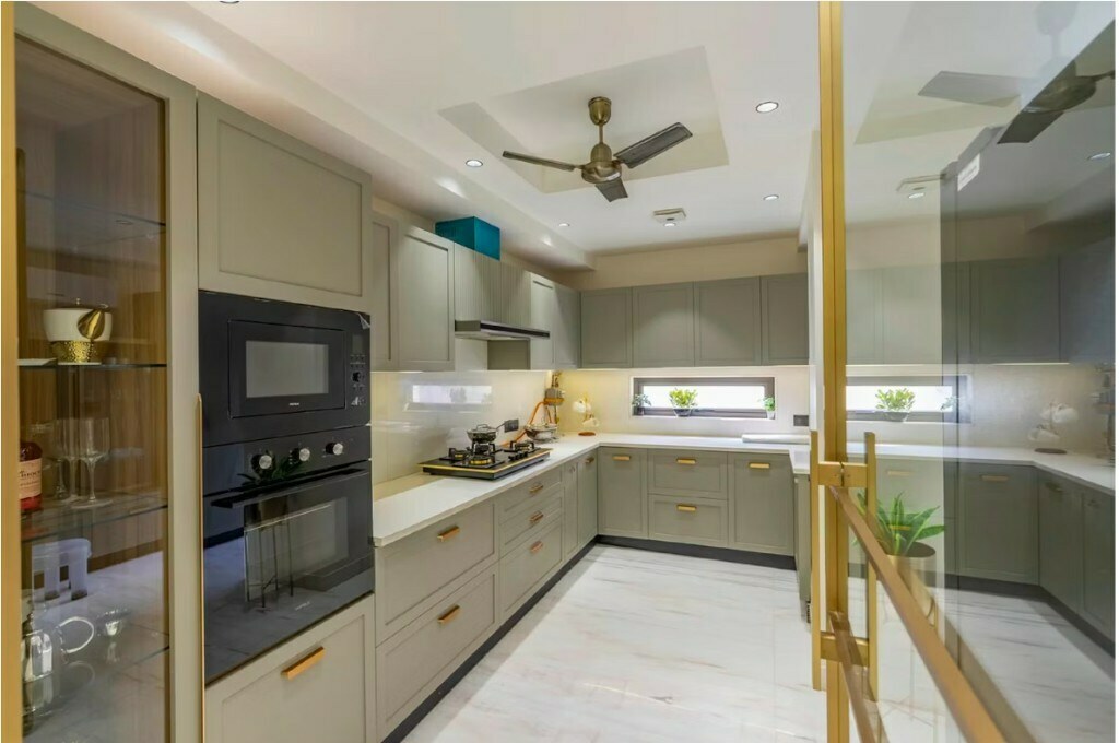Sage green U-shape modular kitchen with gold hardware and glass display cabinet in Delhi home