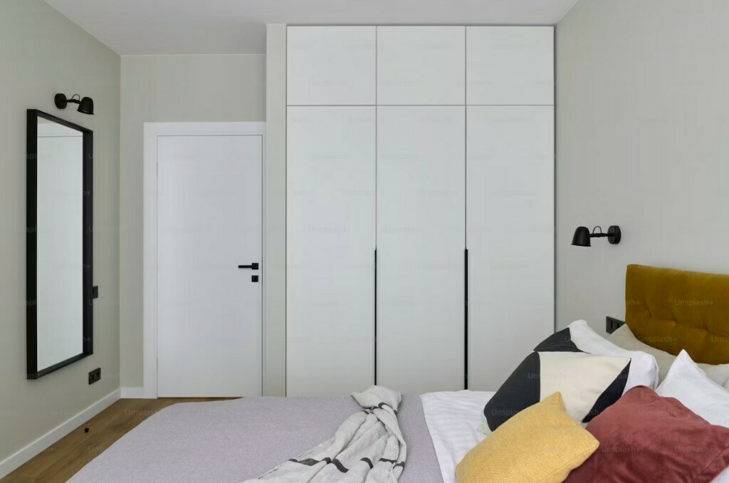 Minimal guest bedroom with white full-height wardrobe and warm accent bedding in Gurgaon apartment